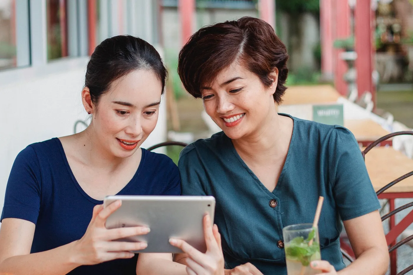 Two women at an outdoor café table looking at a tablet together